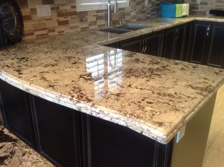 Kitchen countertop with a granite surface, dark-colored cabinets underneath, a stainless steel sink, and a tiled backsplash.