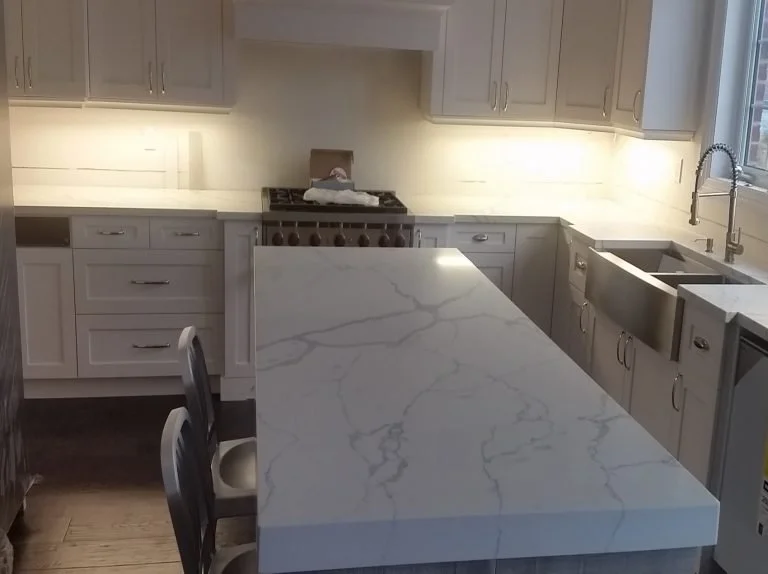 Modern kitchen with white cabinets, marble countertop, stainless steel sink, and a stove with a cardboard box on top.