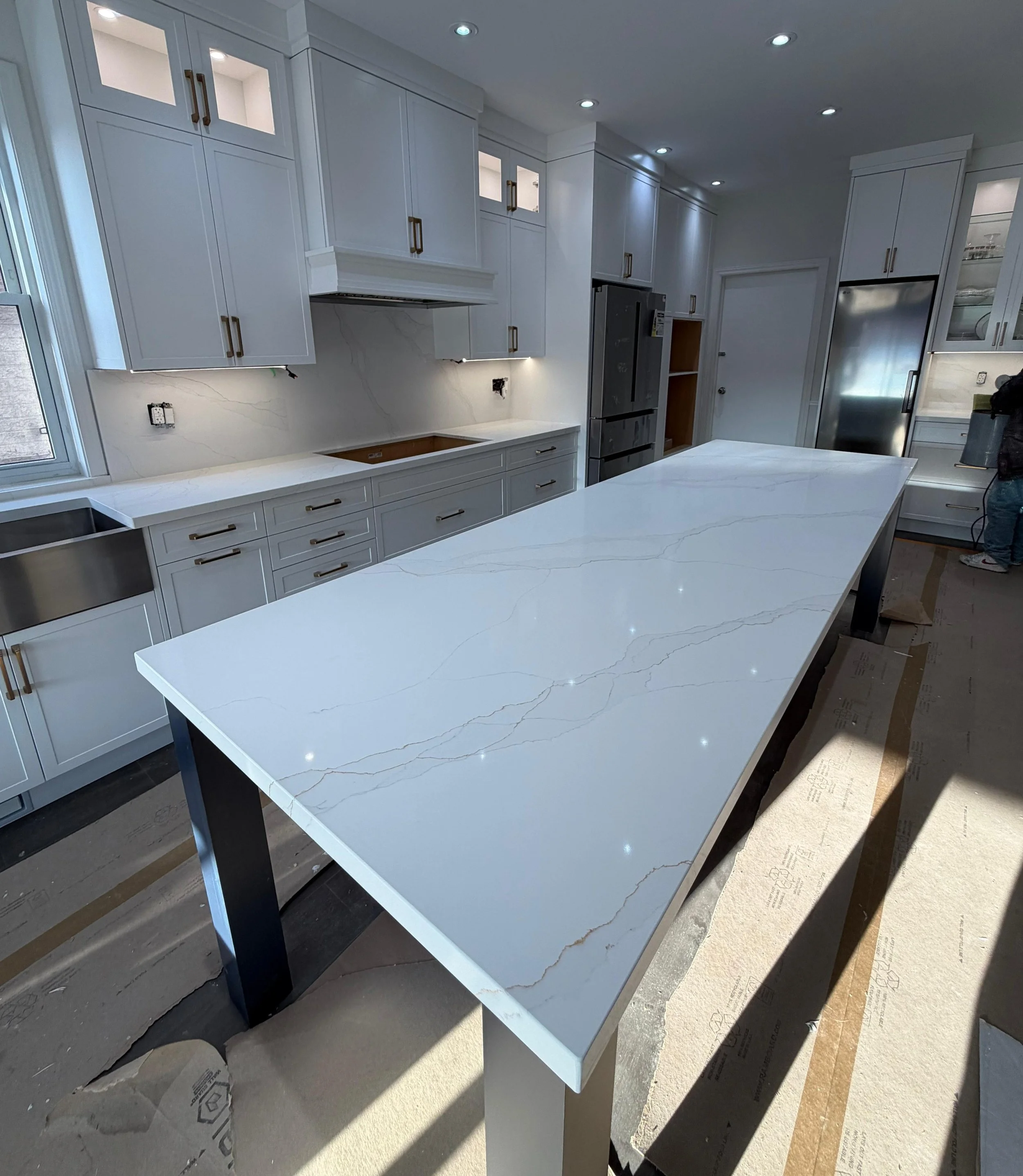 Modern kitchen with white marble countertop island, white cabinets with gold handles, and stainless steel appliances. Some cabinetry and appliances are still under installation in Mississauga.