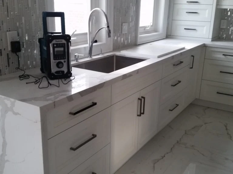 White kitchen countertop with a sink, a small electronic device, and a window above the sink.