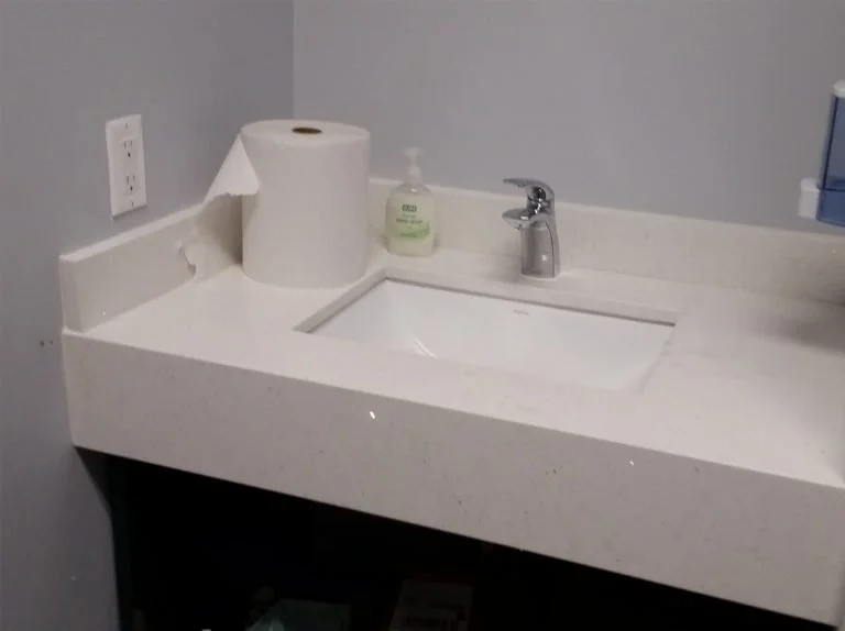 Bathroom sink with a soap dispenser and a roll of toilet paper on the countertop.