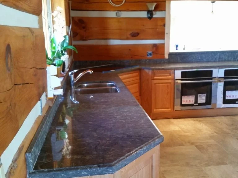 Wooden kitchen with dark granite countertops, sink, and built-in ovens.