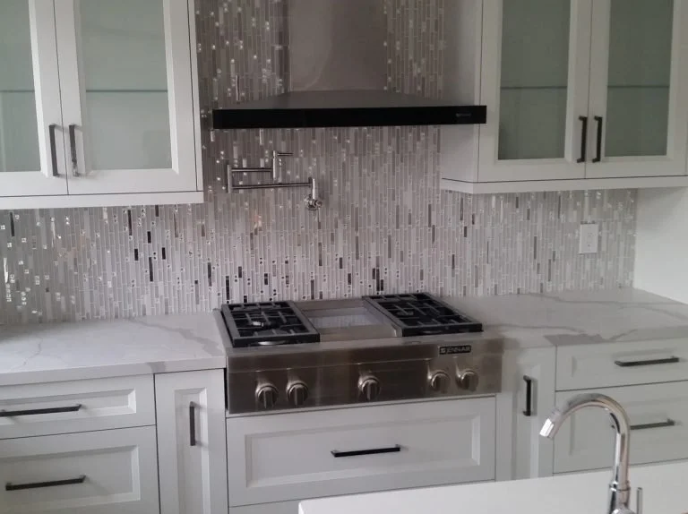 Modern kitchen with white cabinets, a marble countertop, a stainless steel stove, a glass mosaic tile backsplash, and a black range hood.