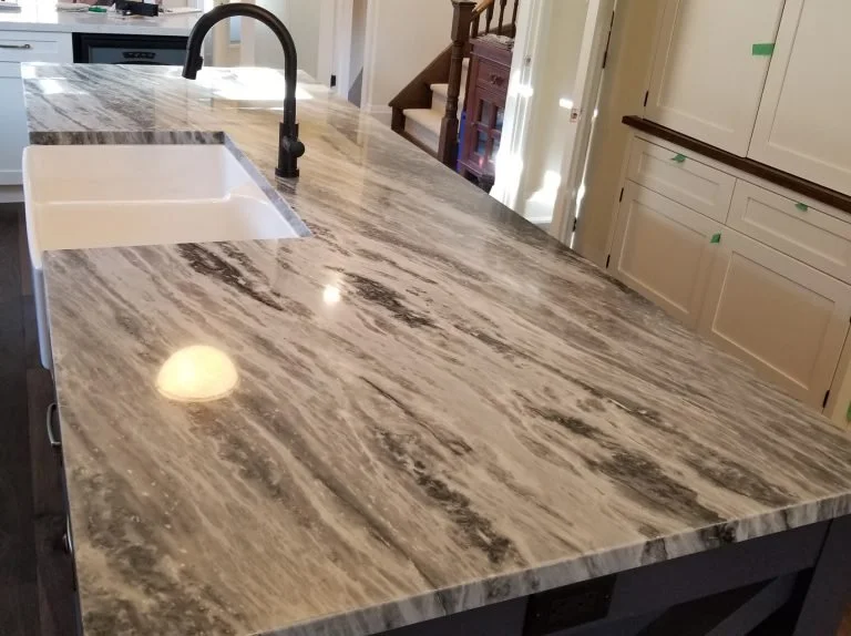 Quartz kitchen island with a white undermount sink and black faucet, beige cabinets with green painter's tape.