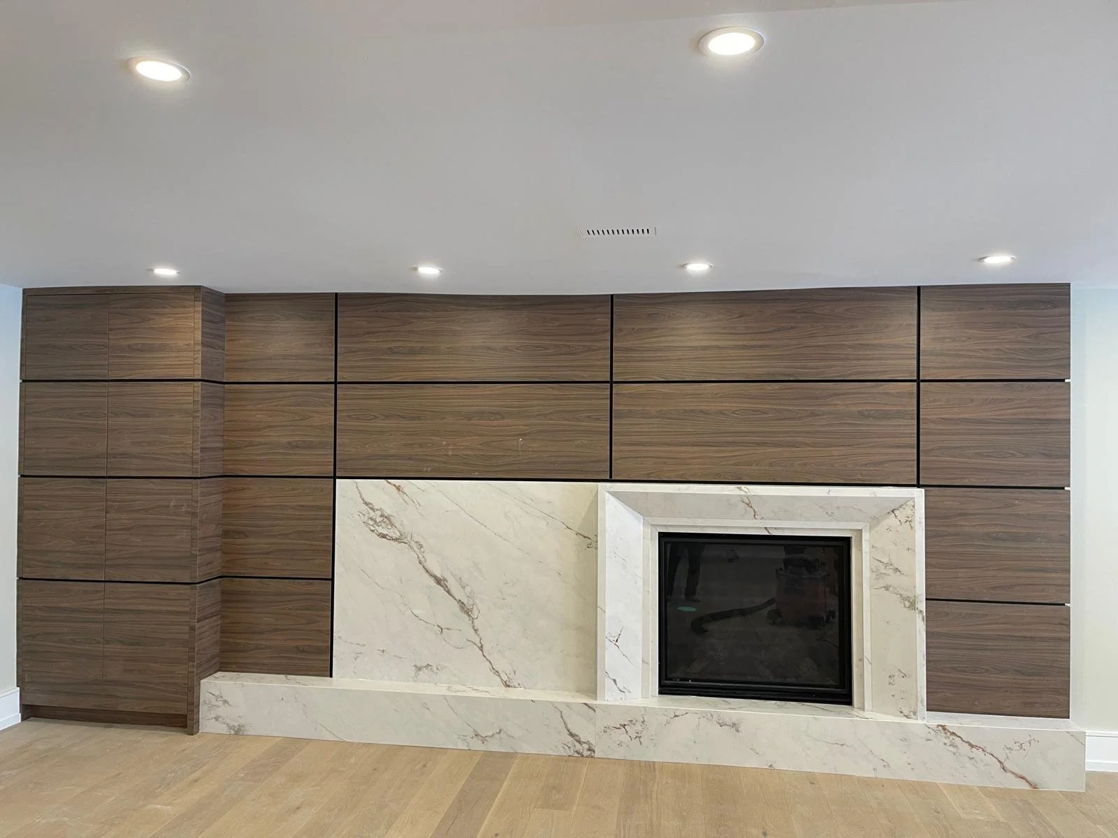 Modern design-forward creative living room fireplace with a white porcelain surround with brown veining, and a walnut wood panel wall background. 