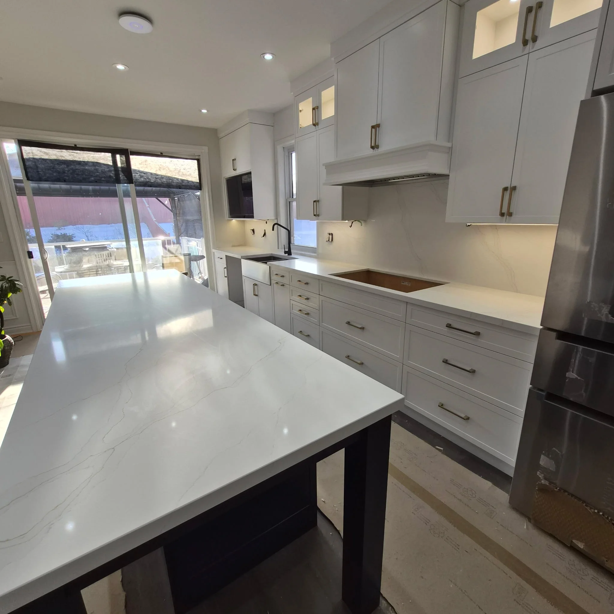 Modern kitchen with white cabinets, marble stone island, stainless steel appliances, and large sliding glass doors letting in natural light in the core of the GTA.