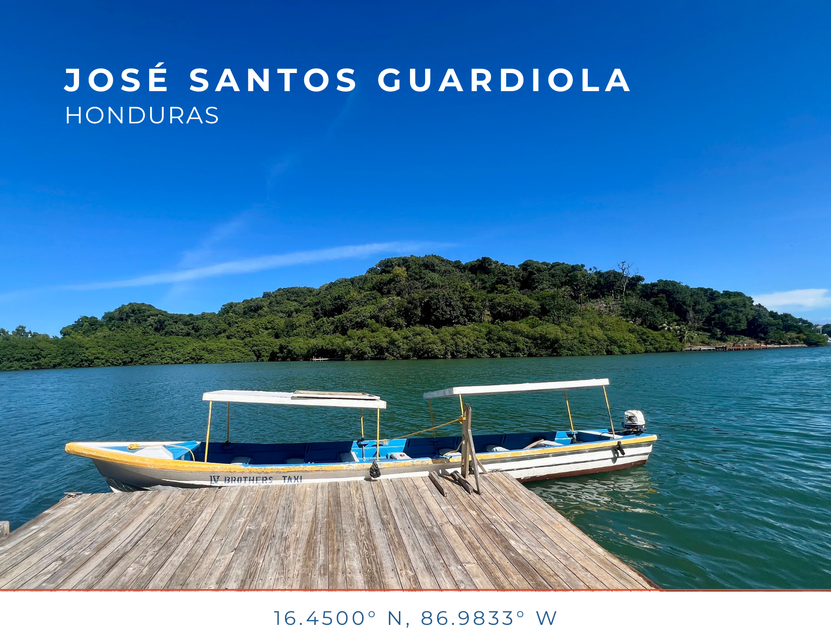 A boat docked at a wooden pier on a lake with a green, forested hill under a bright blue sky.