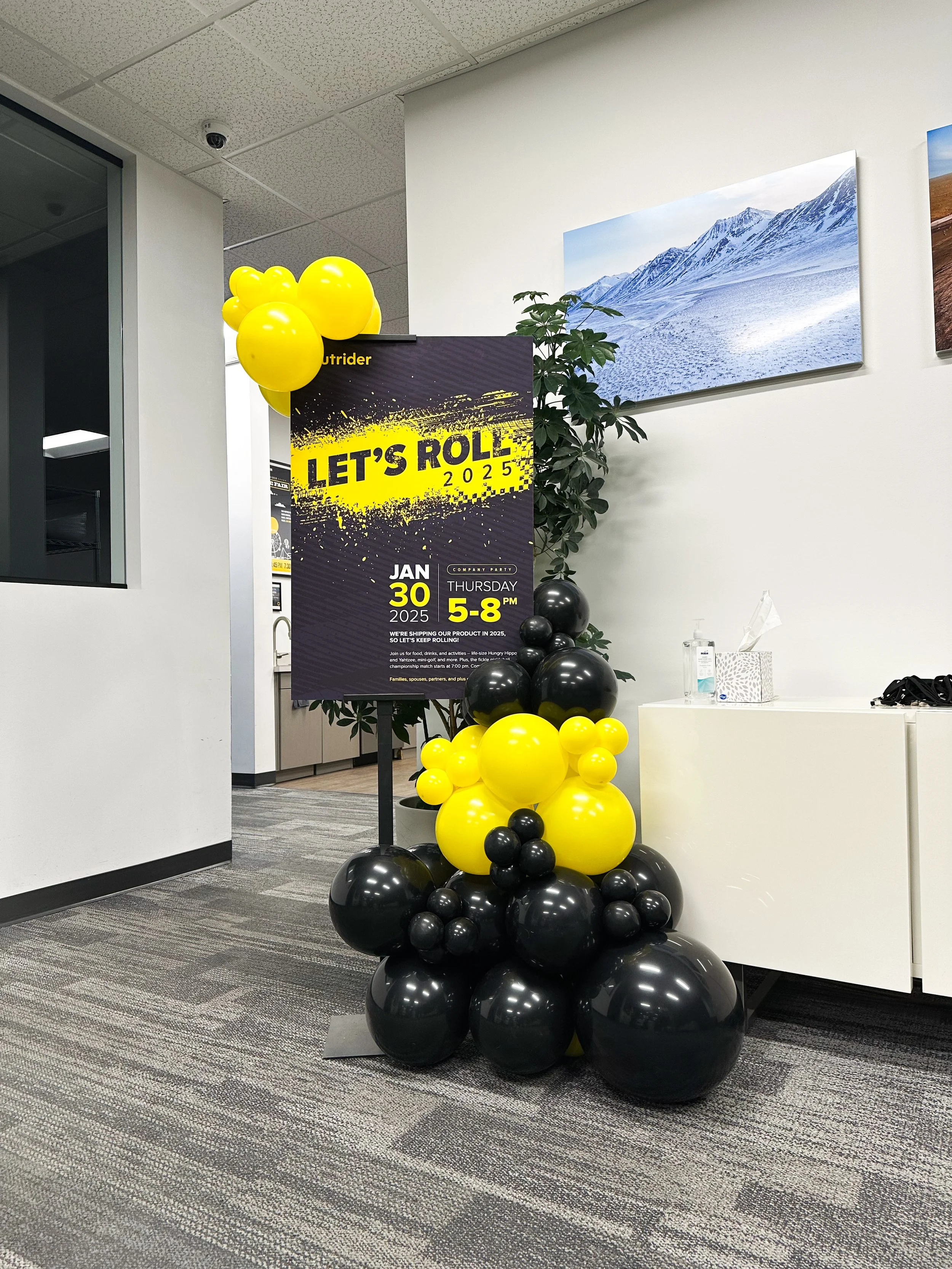 Balloon display with black and yellow balloons, a sign for a company event on January 30, 2025, and a sign for a celebration on Thursday from 5 to 8 PM.