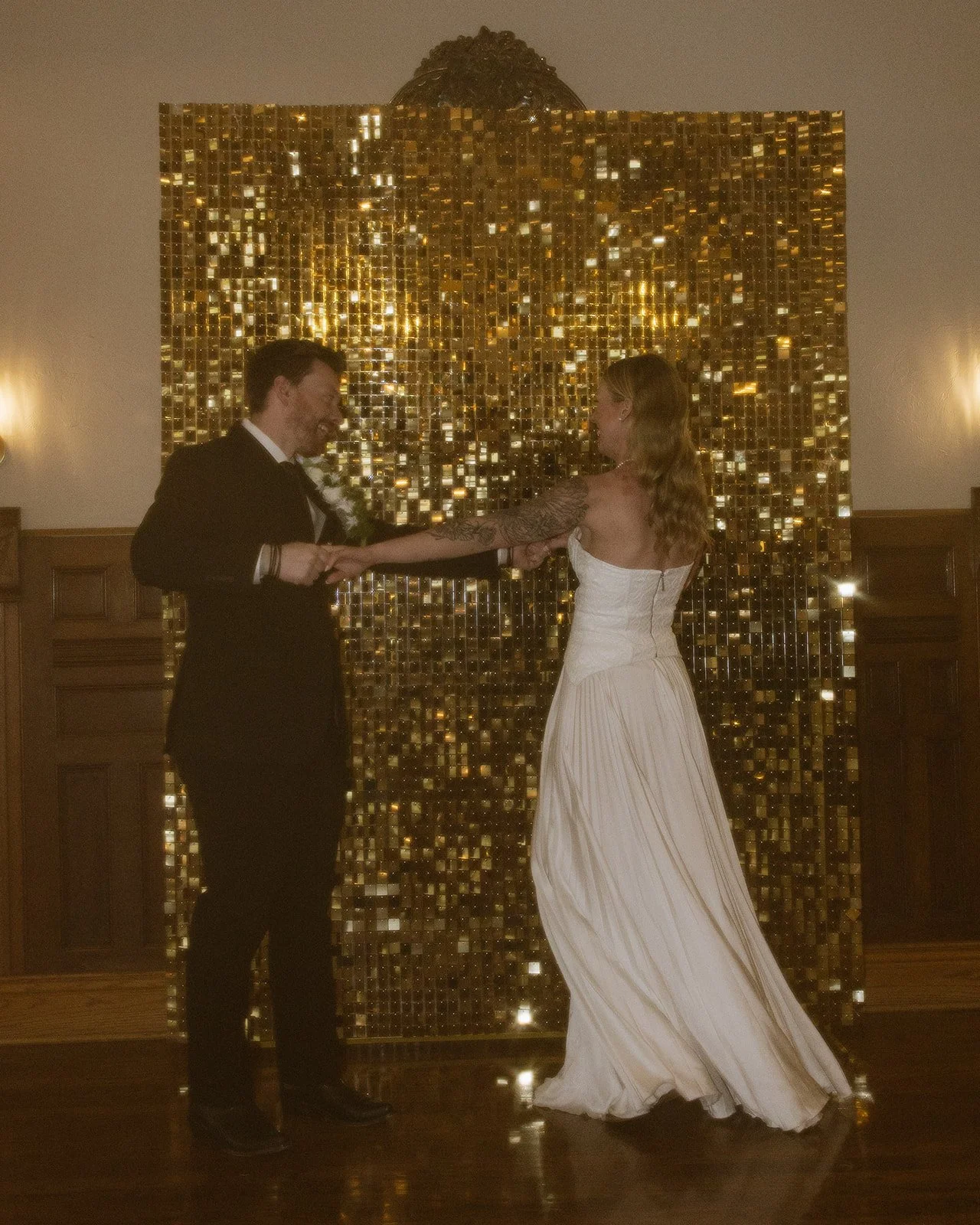 A bride and groom dancing in front of a golden mosaic wall during their wedding reception.