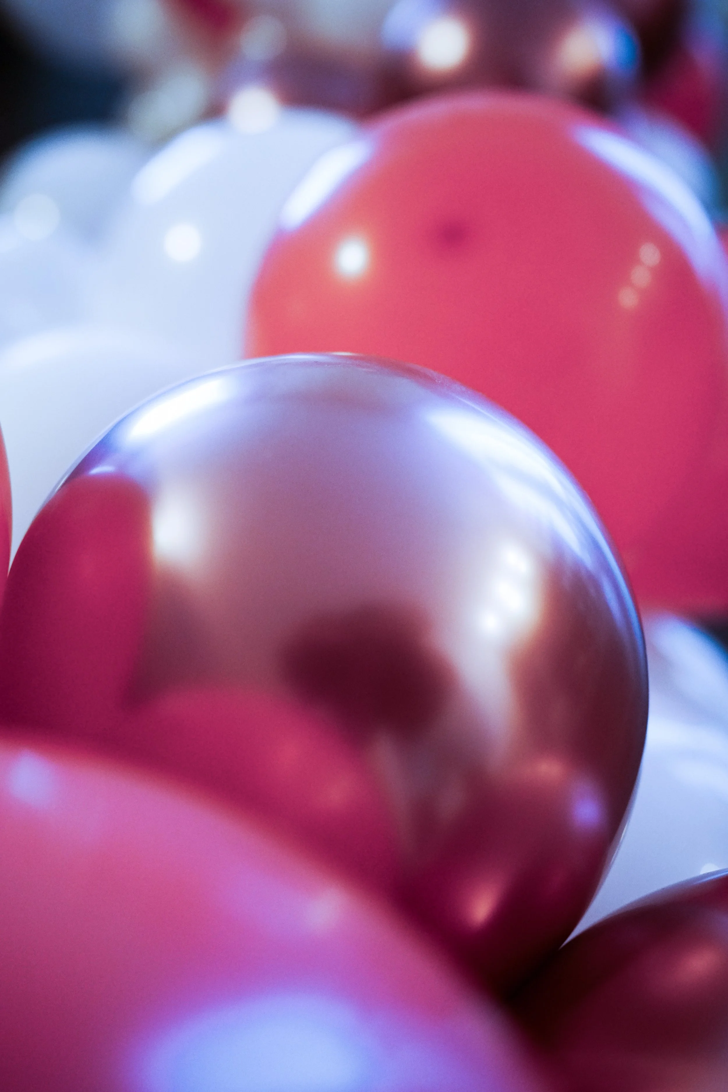 Close-up of colorful balloons in shades of pink, red, and white, with a shiny surface reflecting light.