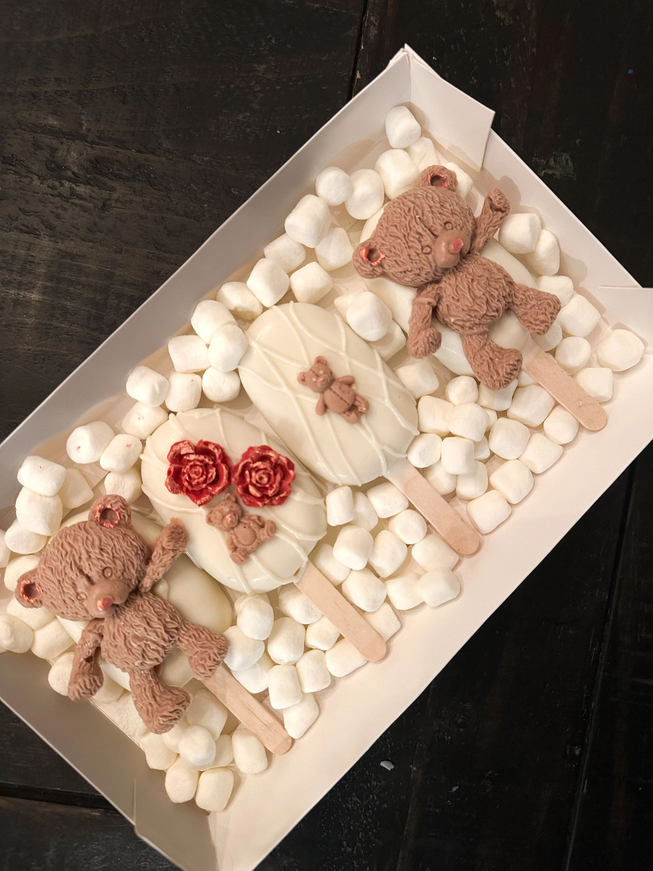 Chocolate bear and teddy bear themed cakepops with white chocolate, surrounded by mini marshmallows in a white tray.