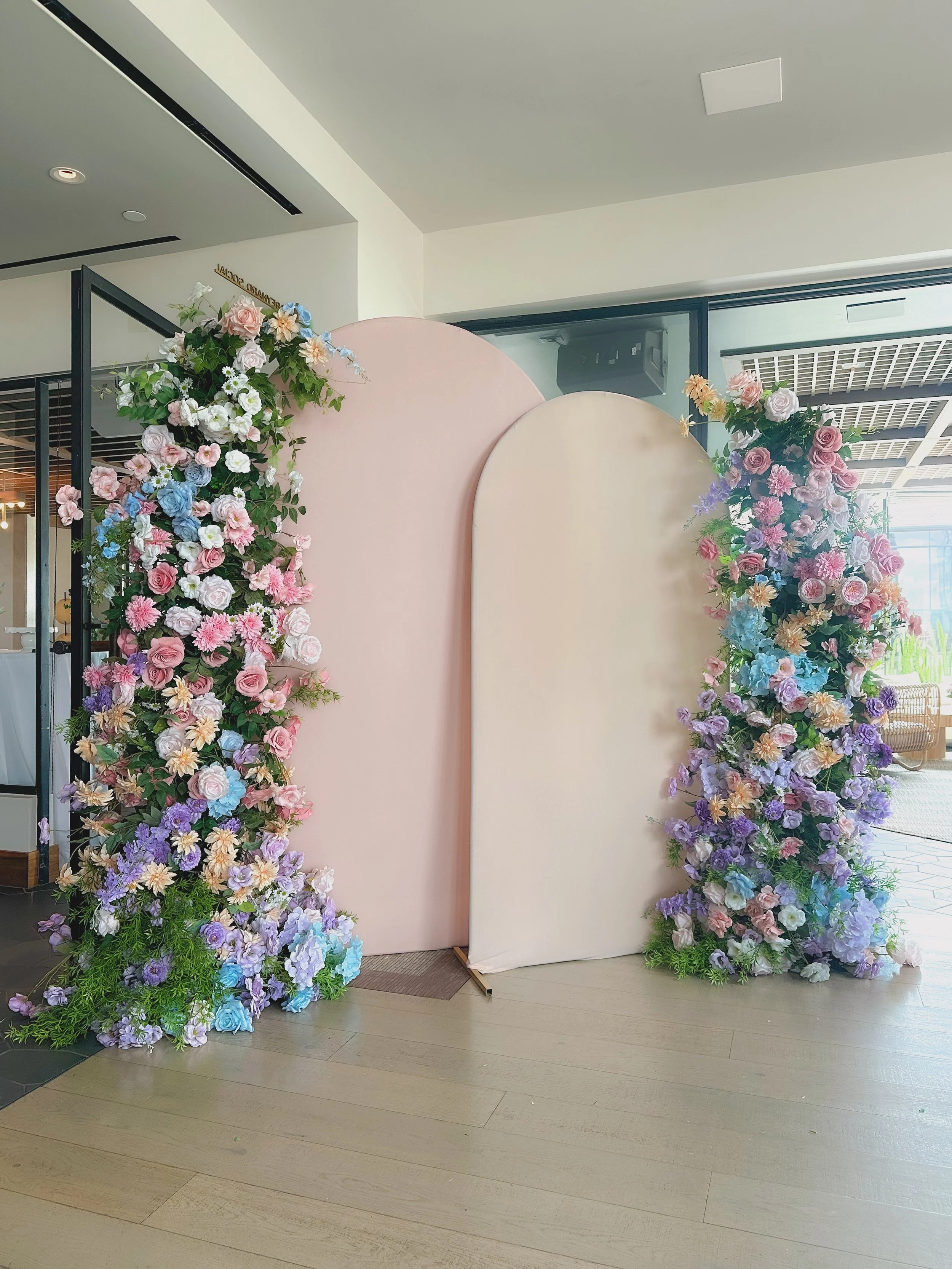 Pink and cream floral wedding backdrop with flower arrangements on either side.