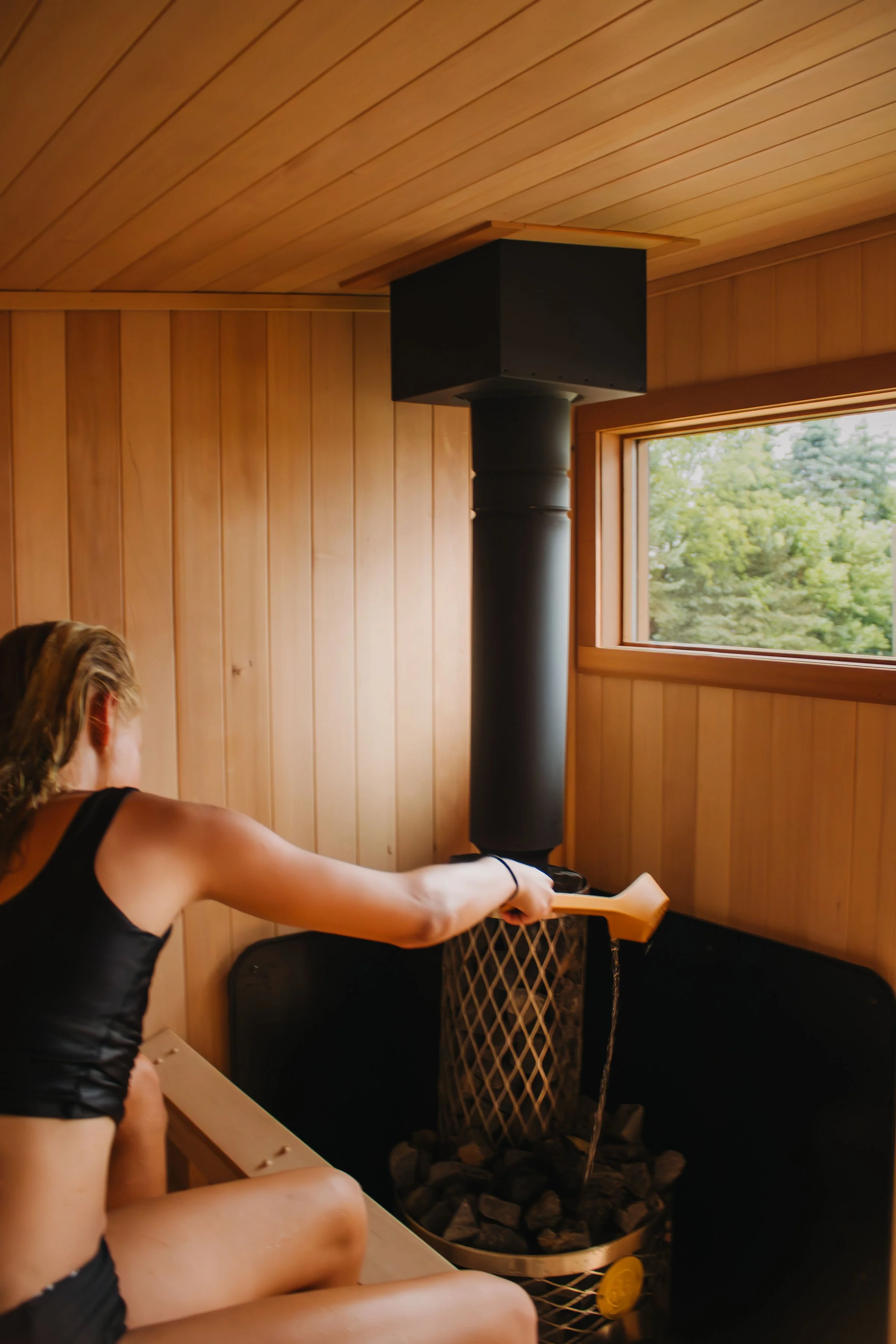 Girl pouring steam in outdoor sauna with Iki wood burning stove