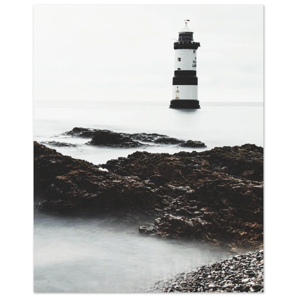 Penmon Point lighthouse above pale water and dark coastal rocks, Anglesey, Wales