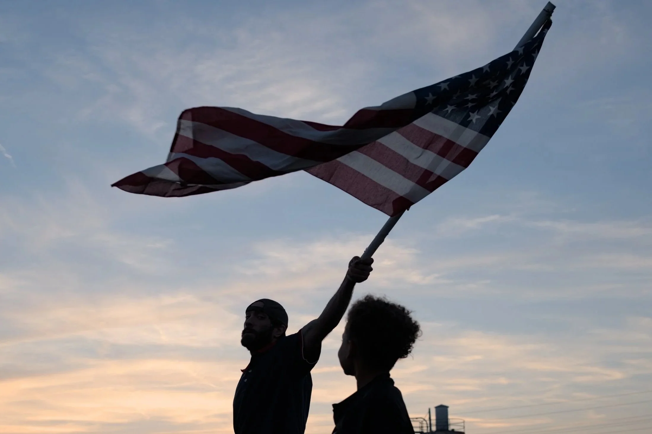 A child watches a demonstrator wave an American flag at a Charlie Kirk memorial hosted by Turning Point USA in Brook Park, Ohio, Sept. 16, 2025. Days before, Charlie Kirk, a conservative activist, was shot and killed. As a co-founder of Turning Point