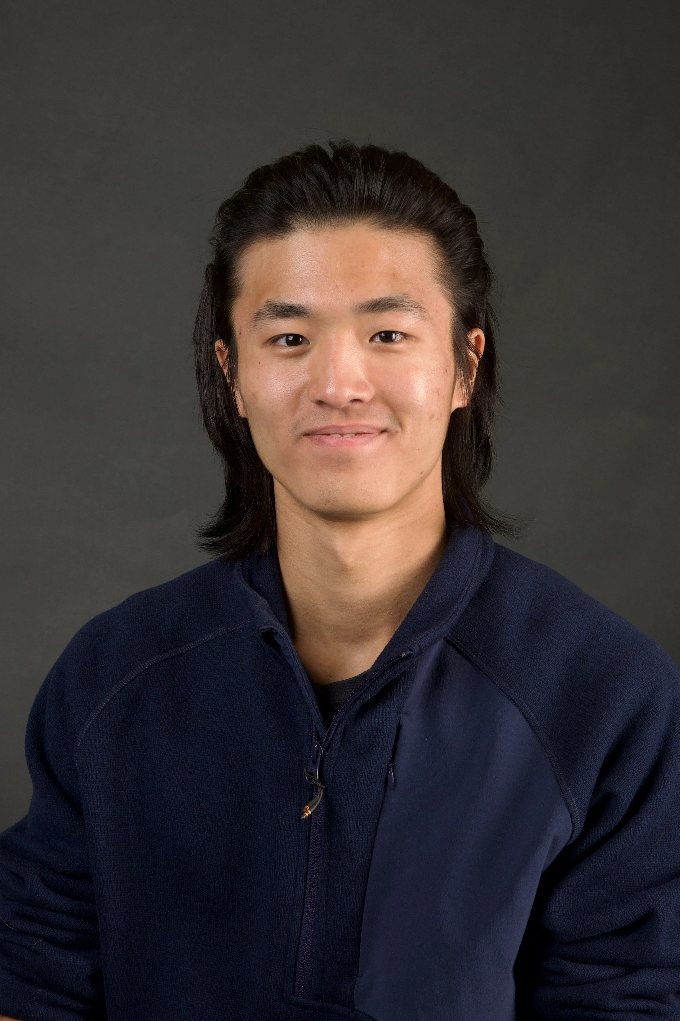 Person in blue pullover, with long dark hair, against gray background.