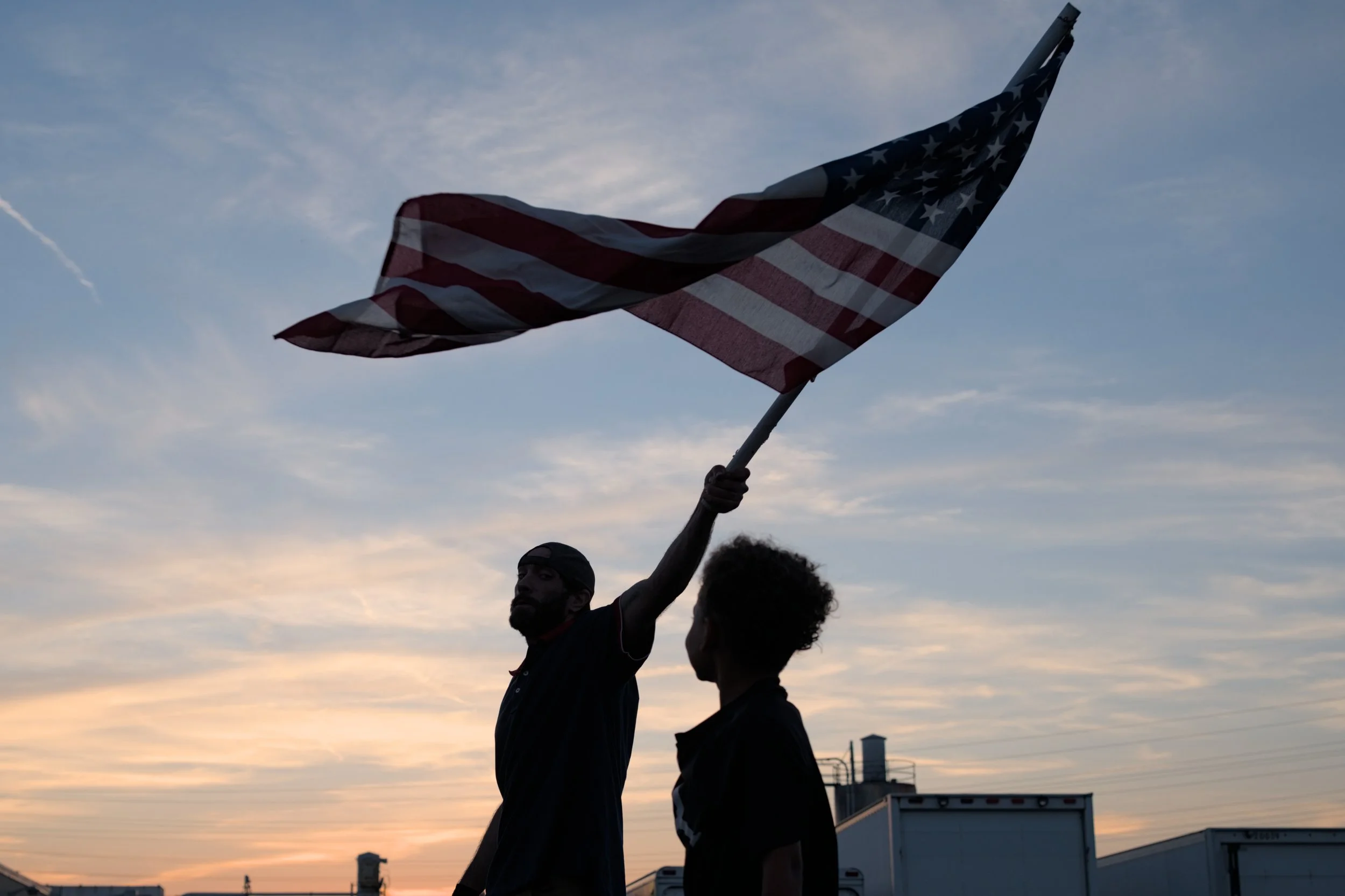 A child watches a demonstrator wave an American flag at a Charlie Kirk memorial hosted by Turning Point USA in Brook Park, Ohio, Sept. 16, 2025. Days before, Charlie Kirk, a conservative activist, was shot and killed. As a co-founder of Turning Point