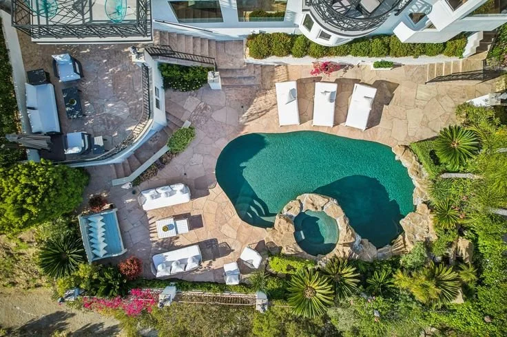 Aerial view of a backyard with a small swimming pool, surrounded by lounge chairs, umbrellas, and lush greenery.