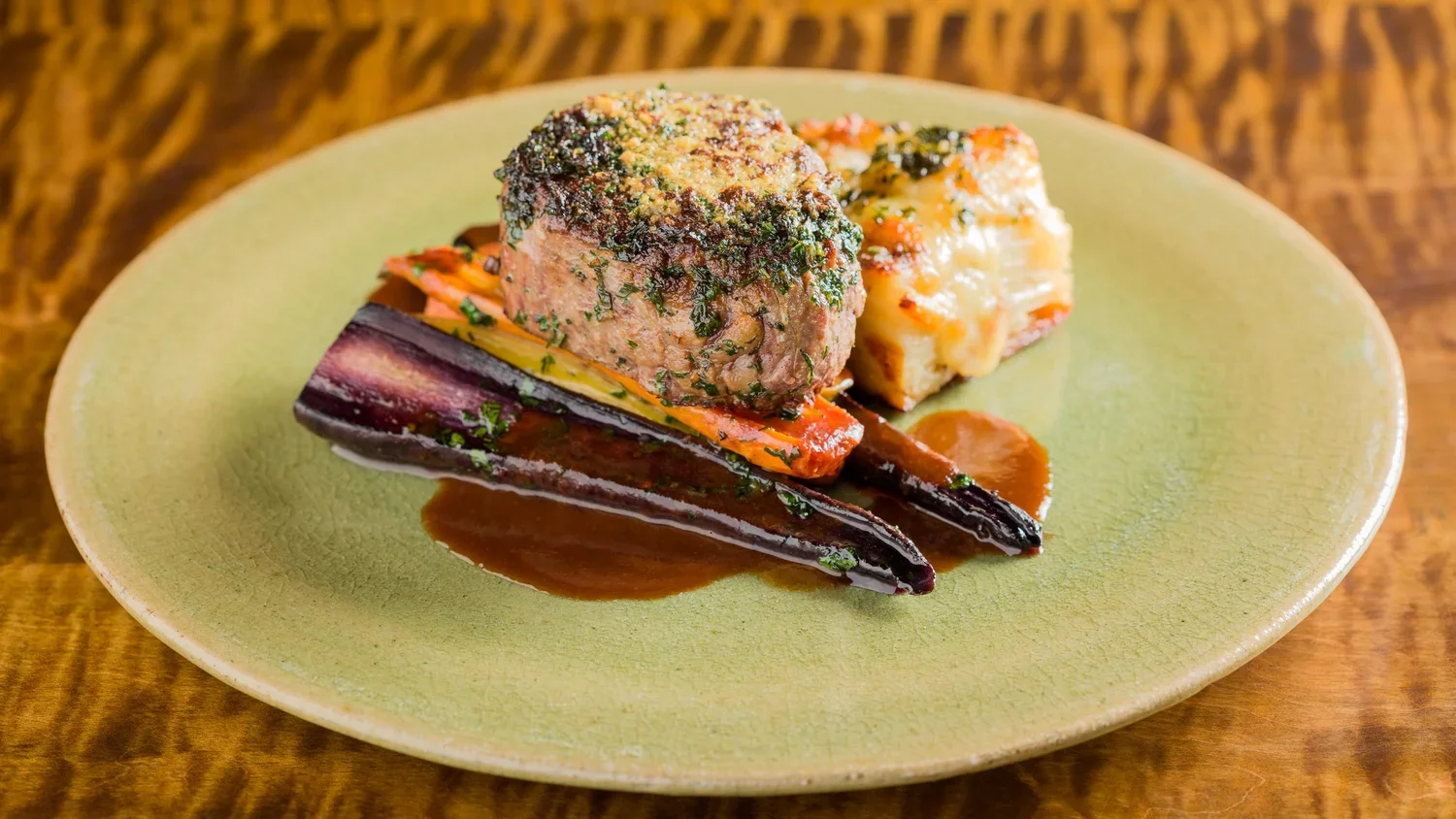 A plate with roasted eggplant, a cooked meatball topped with herbs, and a piece of baked casserole, all served with brown sauce.