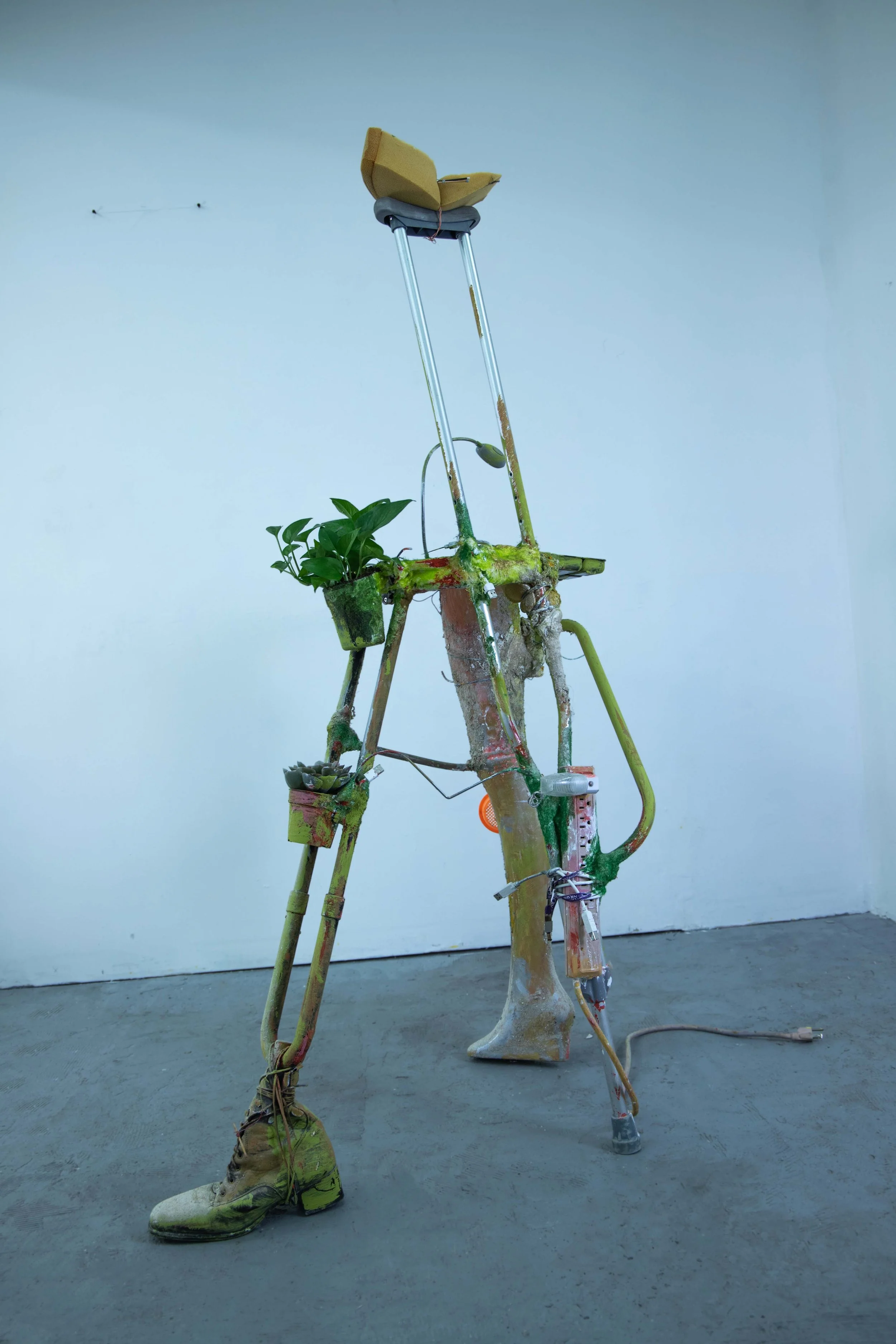 Rosalie Smith
Limping Desk (alternate view)
2025
Crutch, mannequin leg, artificial succulent, light, power strip, boot, desk organizer, foam, beach sifter, lanyard, charging cables, hooks, artificial grass, plaster, debris, PVA glue 
62 x 30 x 20 in.