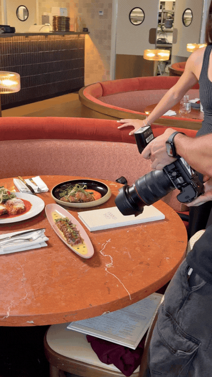 Photographer taking pictures of Japanese dishes on a restaurant table, including sushi and a salad.