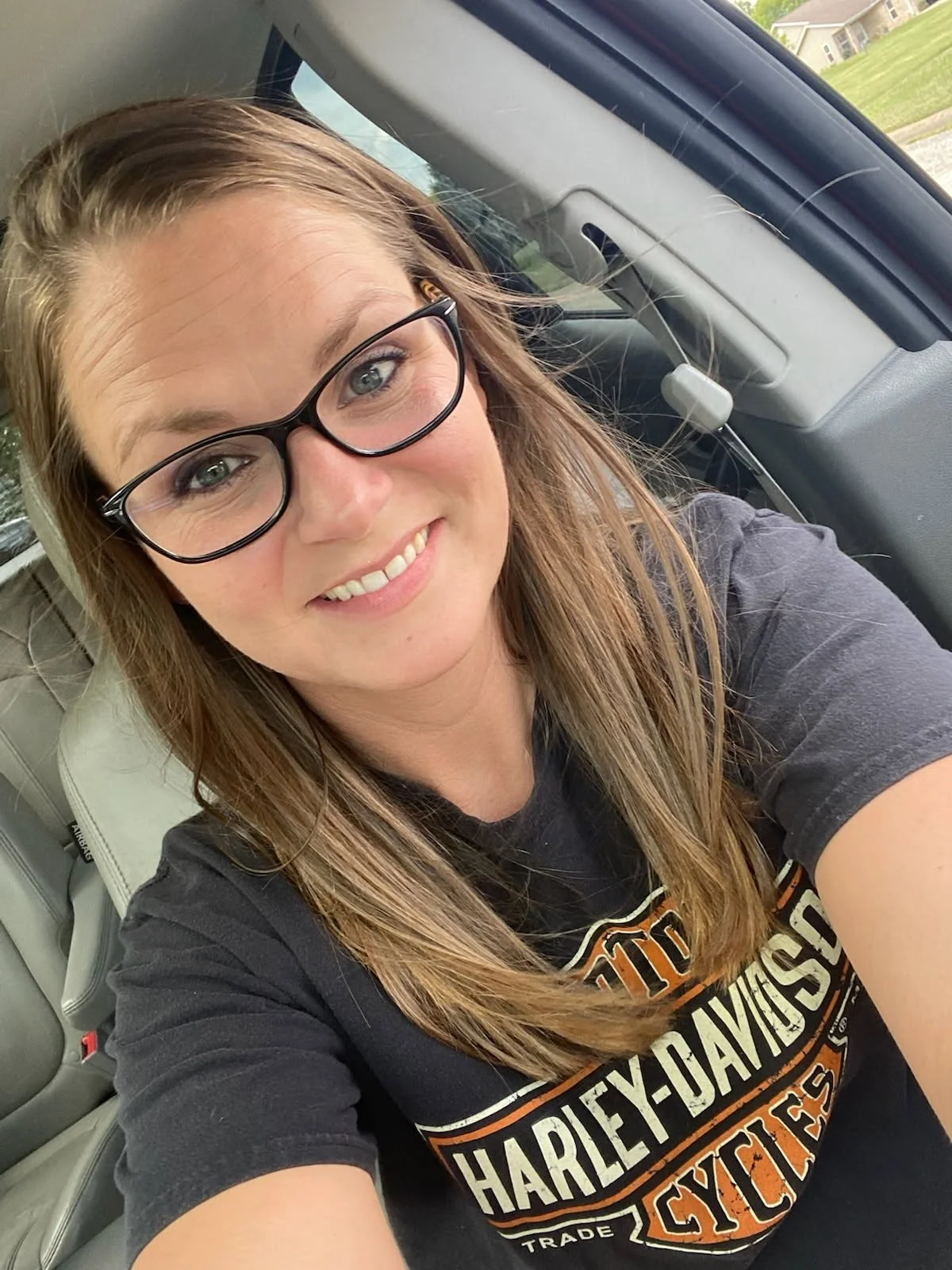 Close-up of a woman smiling with makeup, wearing a striped shirt and a necklace, with dark hair.