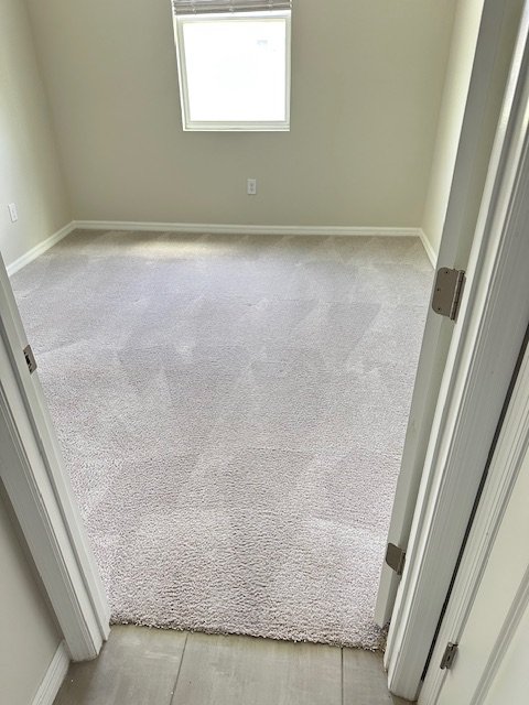 Empty beige room with carpeted floor, window, and door frame