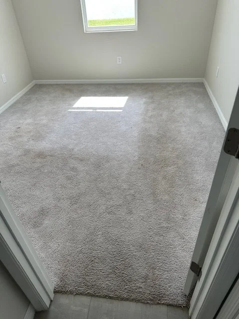 Empty room with grey carpet and a small window letting in natural light.