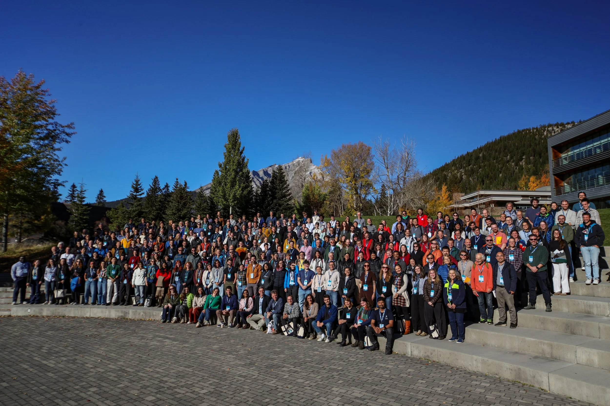 300+ IPICS attendees standing together on a sunny clear day, with the mountains and trees of Banff in the background