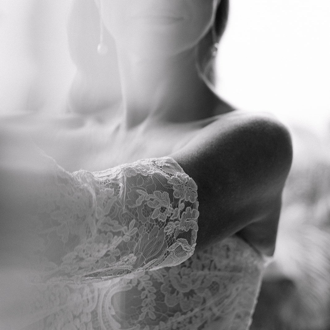 Close-up black and white photo of a woman in lace dress, highlighting her shoulder and part of her face and neck.