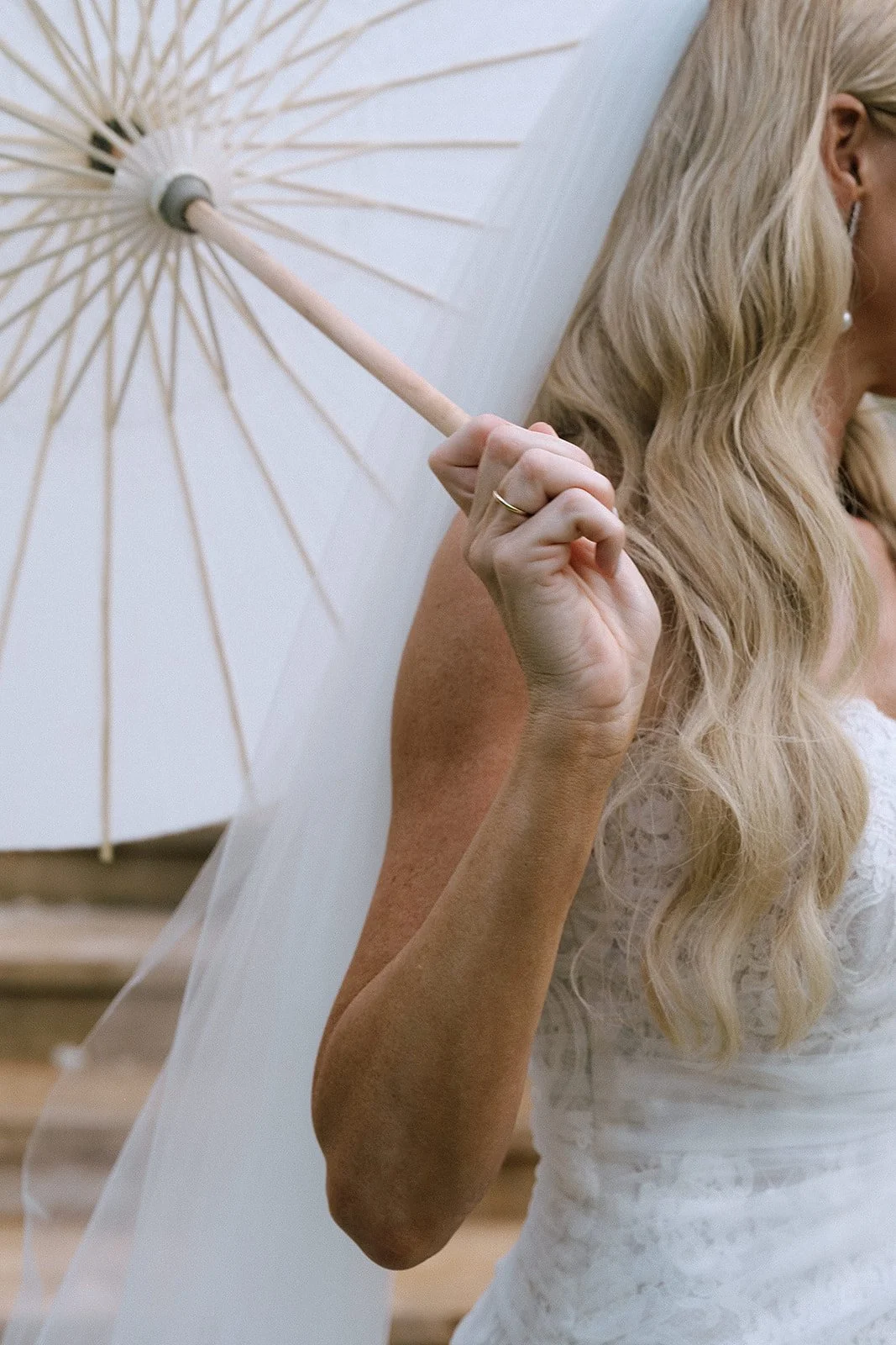 A woman with blonde hair holding a white parasol, wearing a lace white dress.