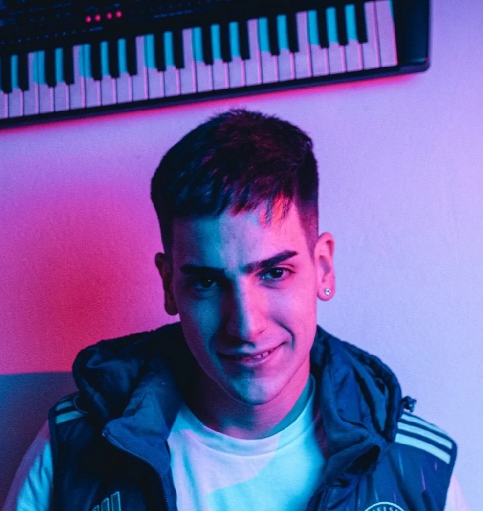 FAKKA DJ sonriendo bajo luces de colores con un teclado musical en la pared.