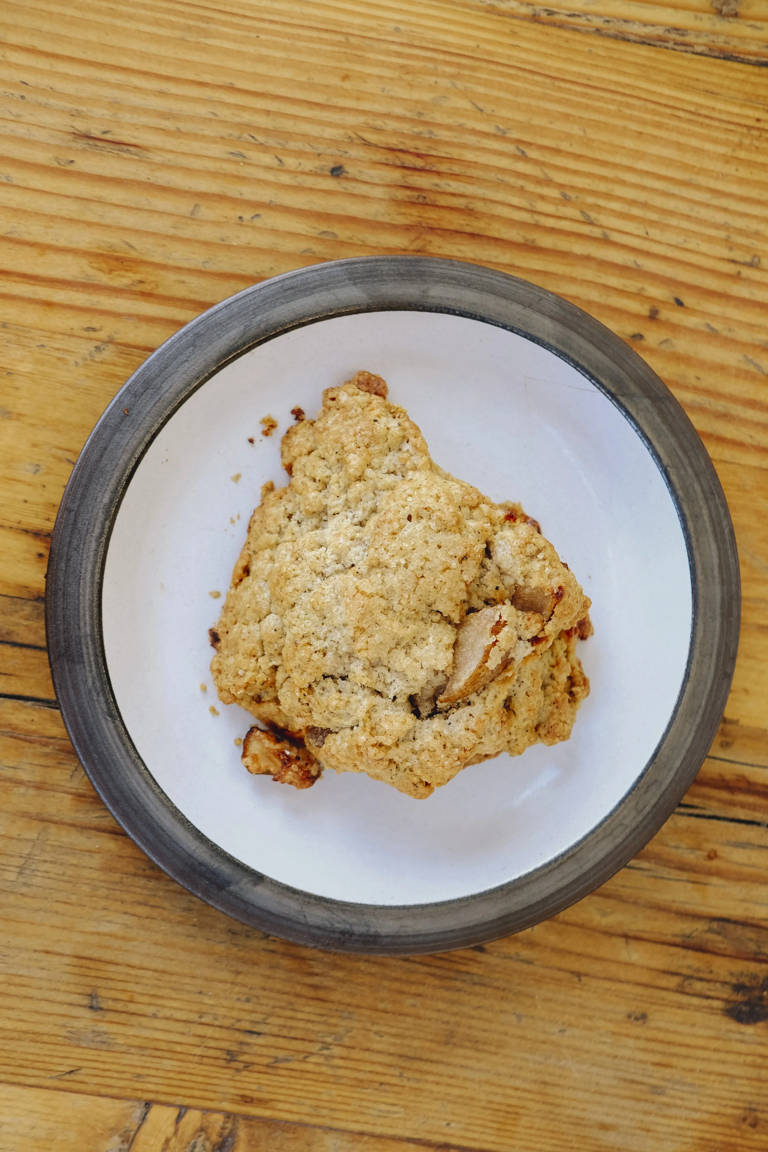 A freshly baked chocolate chip cookie on a white plate with a black rim, placed on a wooden table.