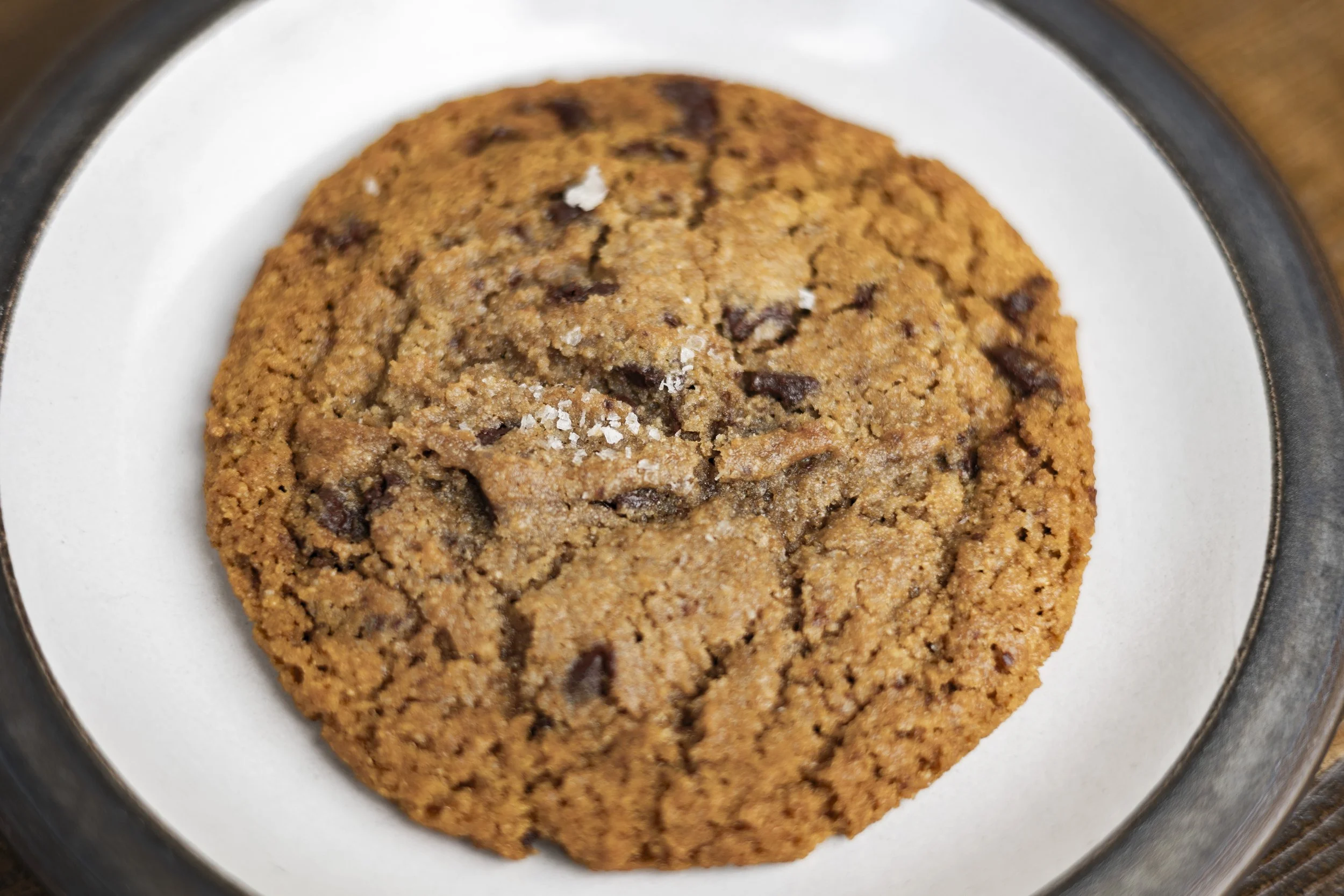 Chocolate chip cookie on a white plate with a black rim.