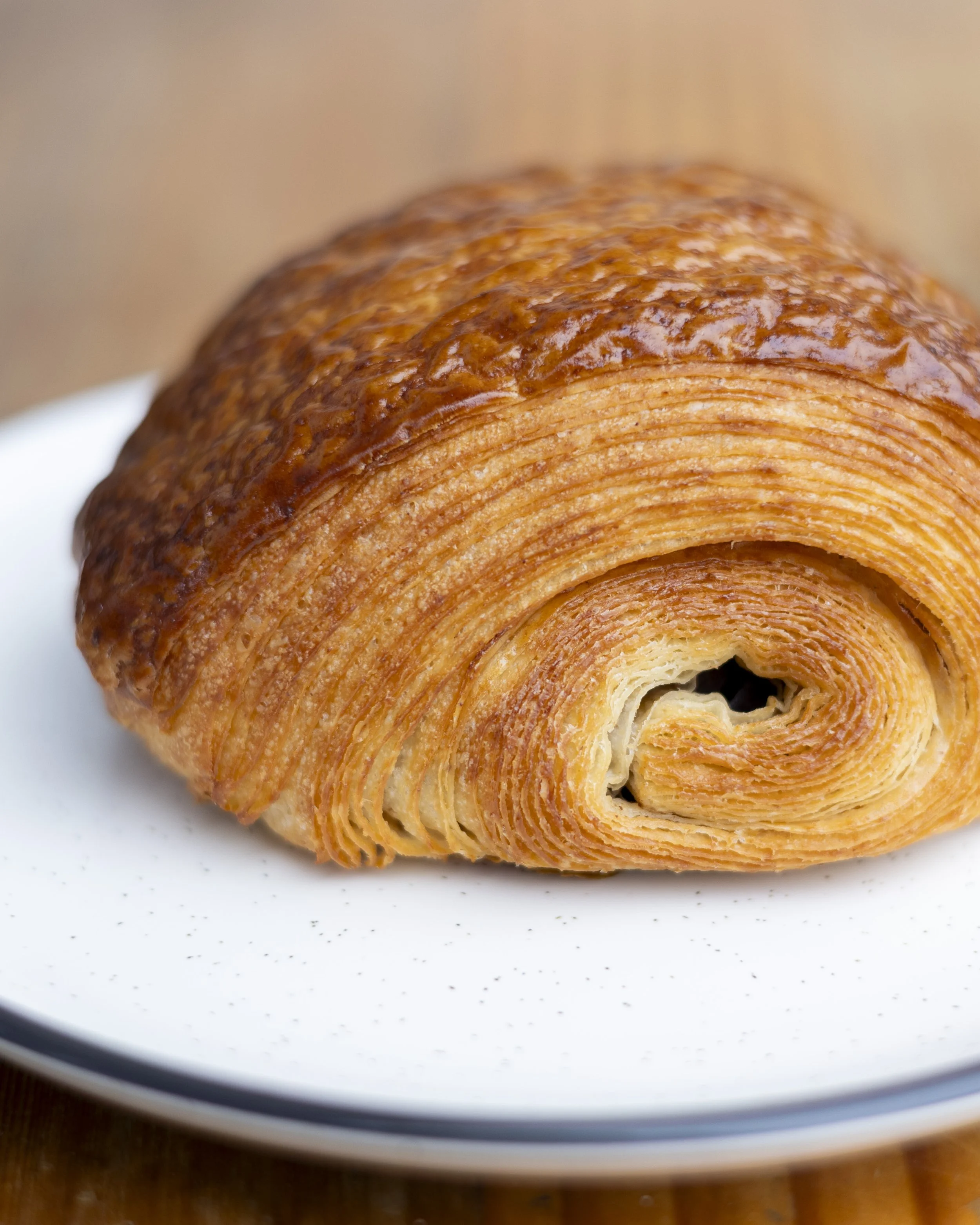 A close-up of a golden-brown croissant on a white plate.
