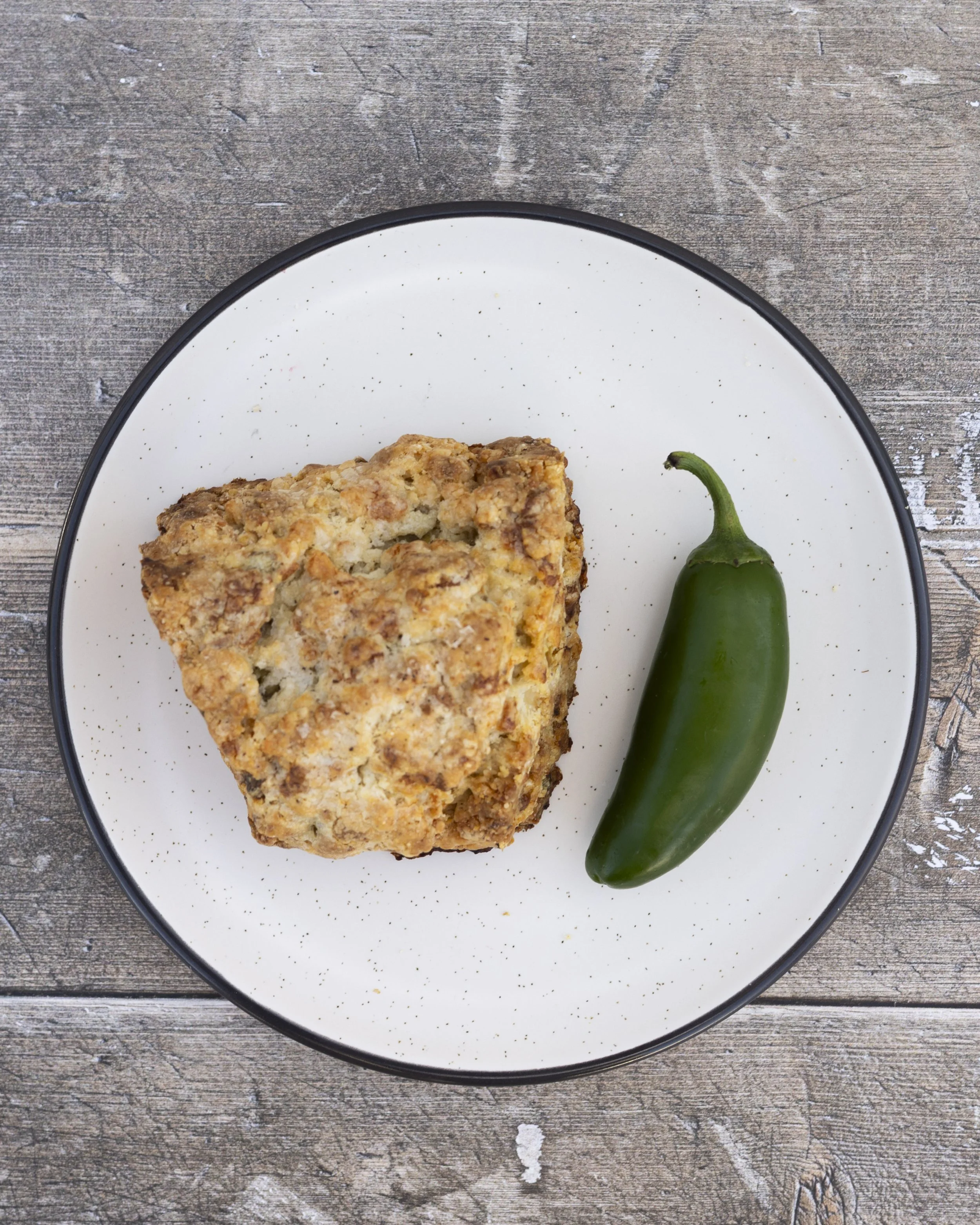 A plate with a slice of cake and a jalapeño pepper on a wooden surface.
