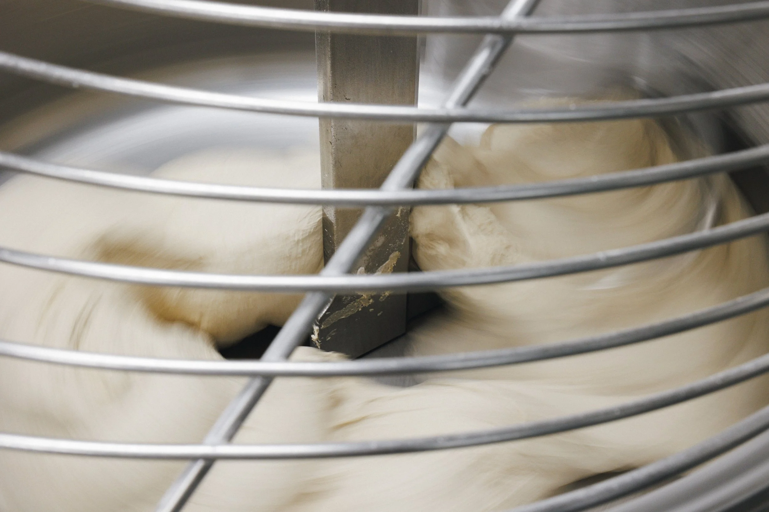 Close-up of dough being mixed or kneaded inside a stand mixer with metal wire guard.