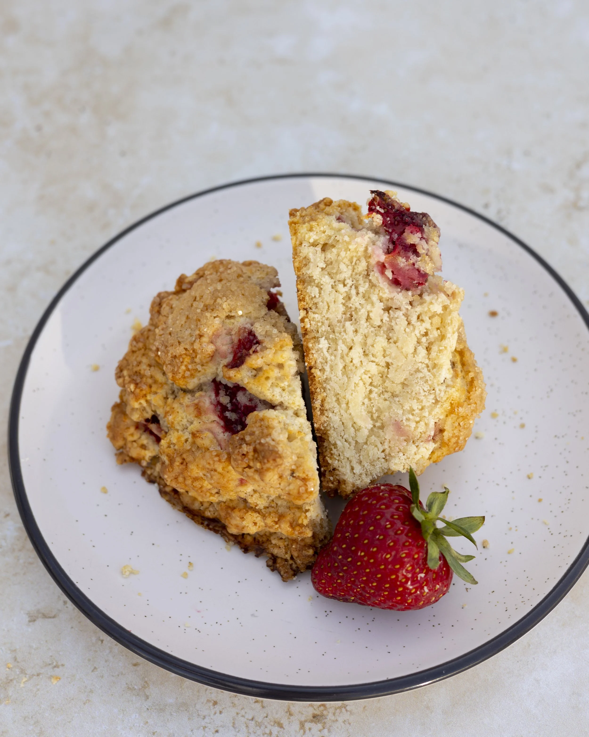 A slice of strawberry scone on a white plate with a strawberry on the side.