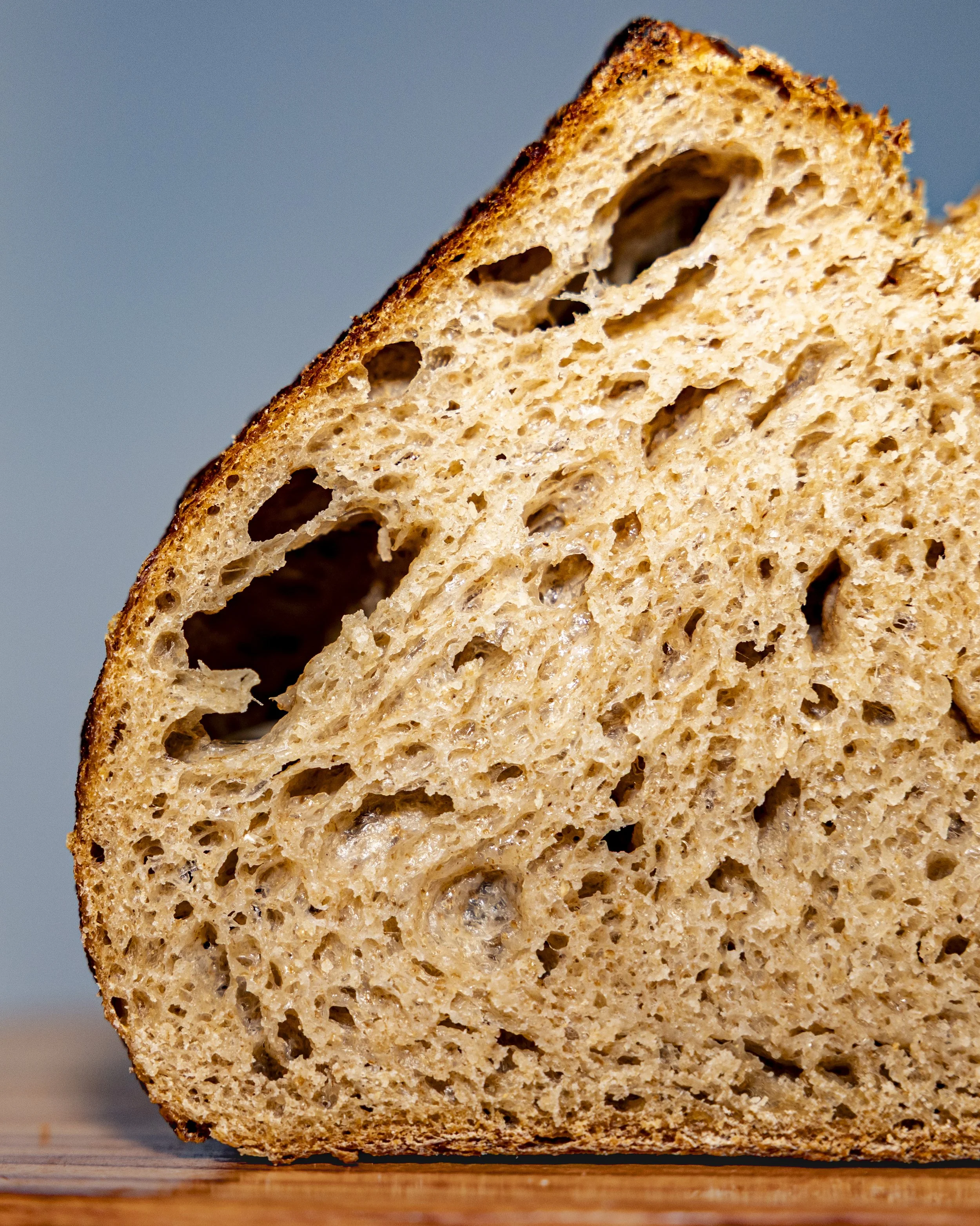 Close-up of a slice of whole wheat bread with a soft crumb and a browned crust, placed on a wooden surface.