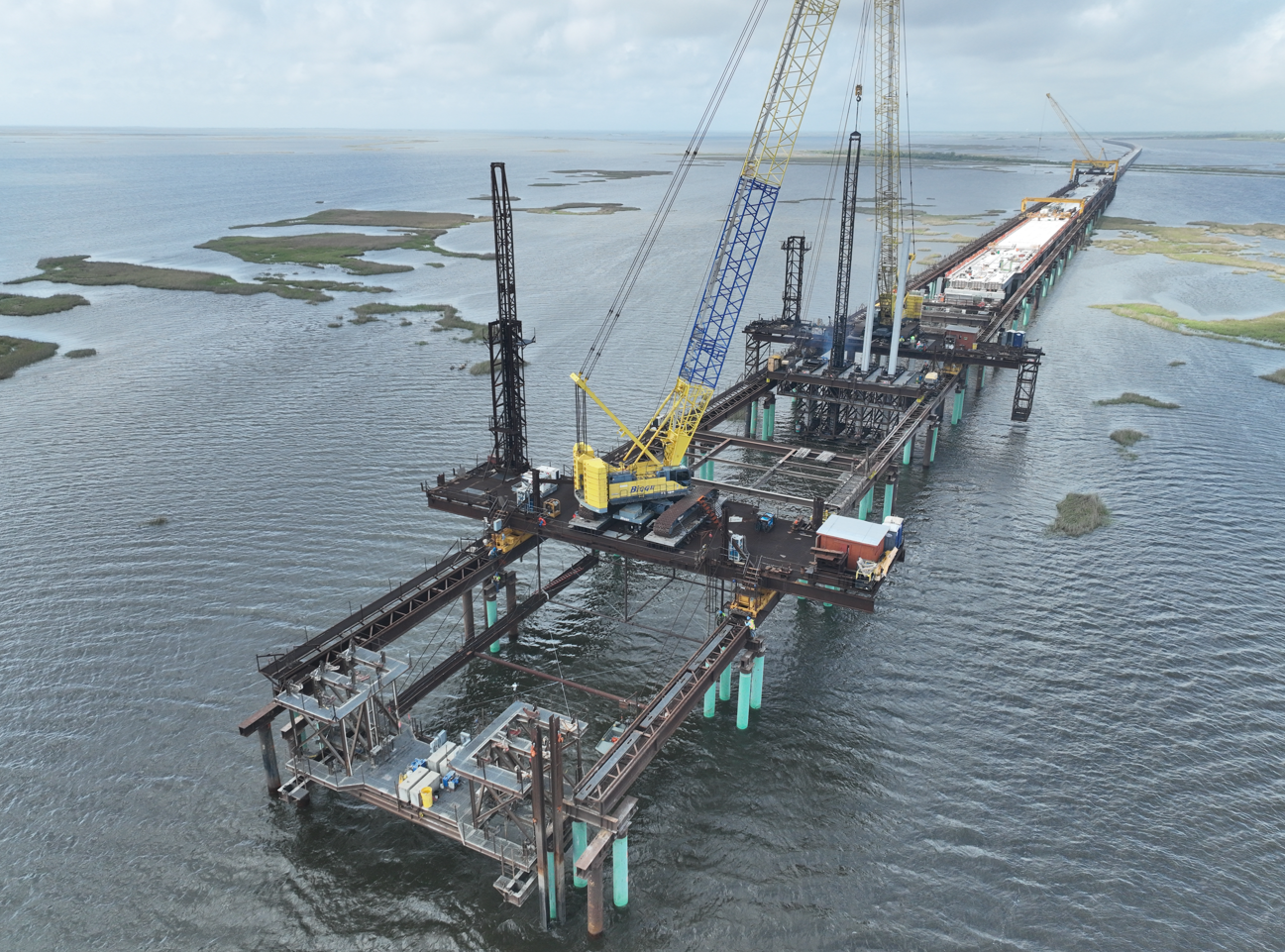 Offshore oil rig construction platform with cranes over water, with land and small islands in the background.