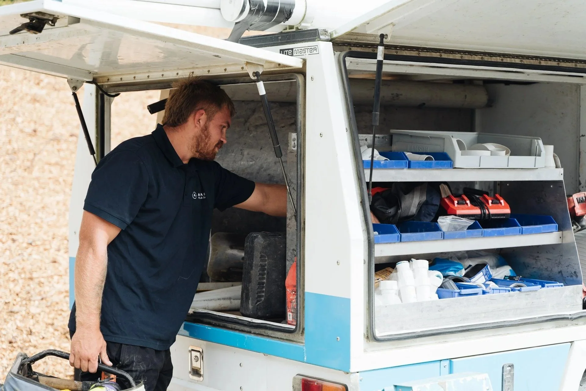 A man working on a mobile utility vehicle with shelves filled with tools and supplies.