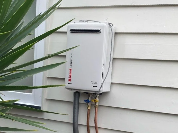 A person installing or repairing a carbon monoxide detector on an outdoor wall near wooden fencing.