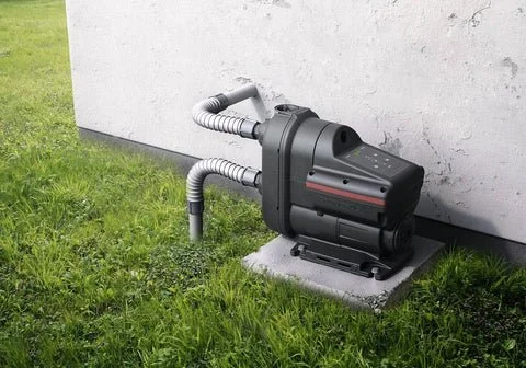 A grey Puretec Hybrid G Series water filtration system mounted on a black brick wall outdoors, with plumbing pipes and valves nearby.