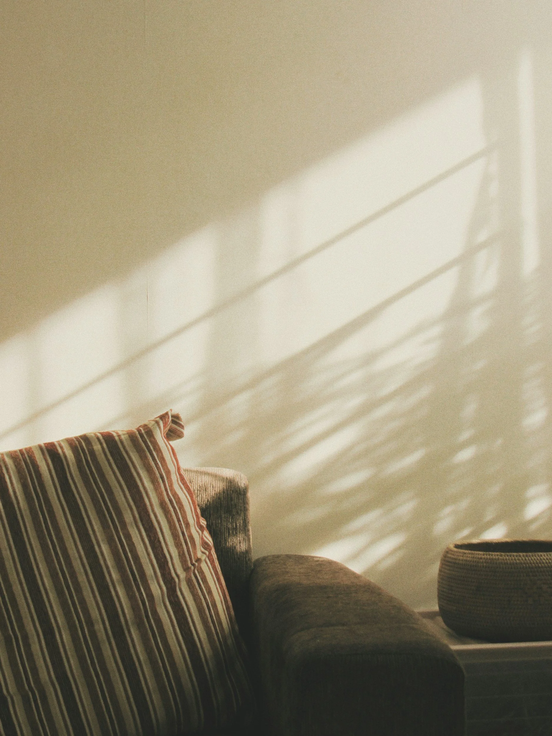 Warm sunlight casting soft shadows on a wall next to a cozy couch in a therapy office.