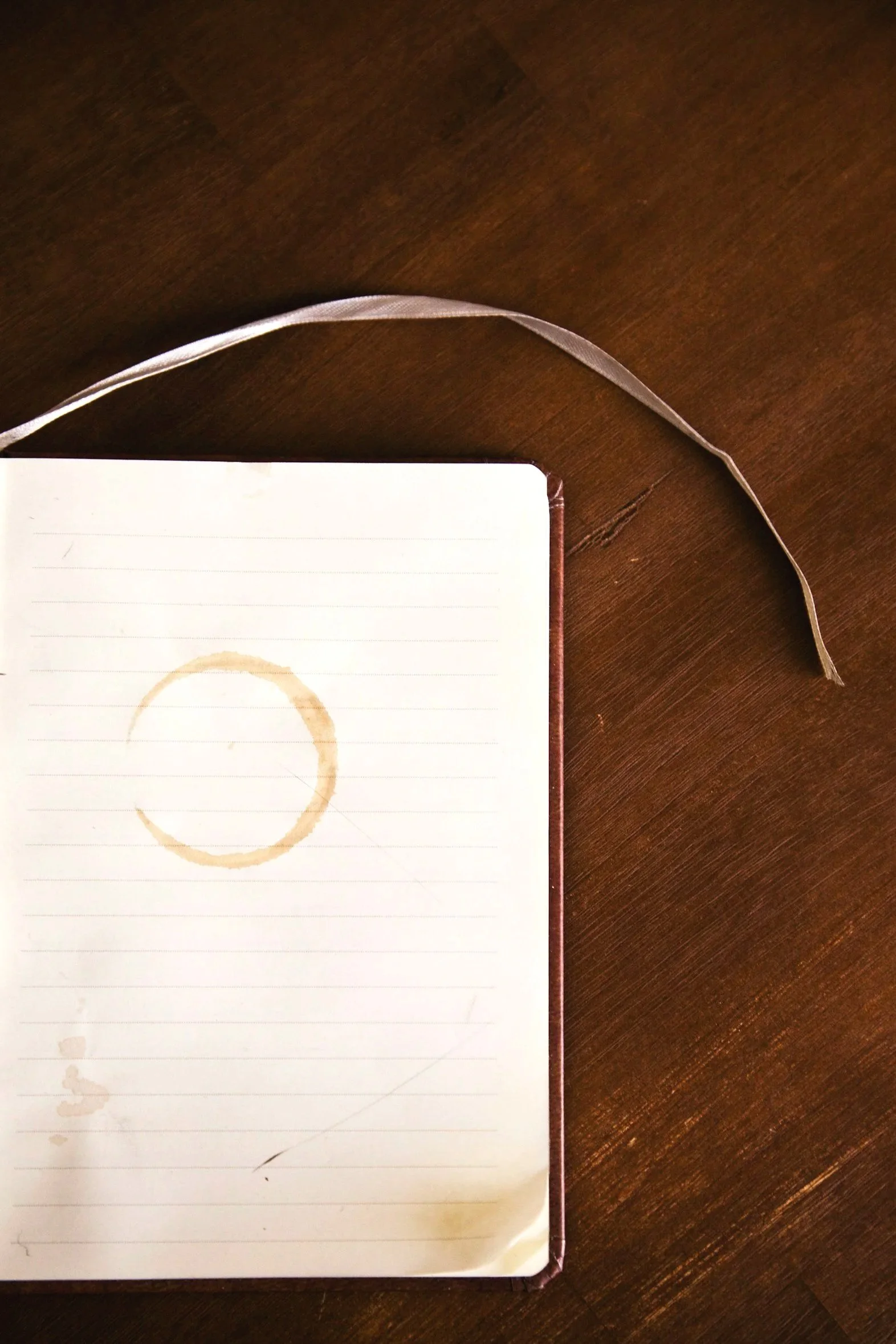 Open lined journal resting on a dark wooden desk with a circular coffee mug stain.