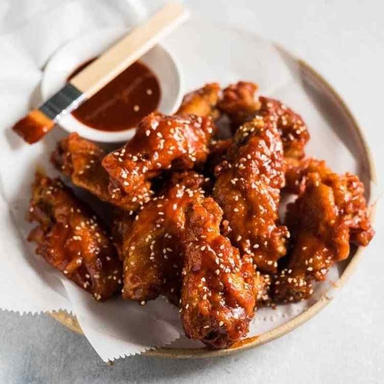 Plate of Korean fried chicken wings with sesame seeds and sauce on the side