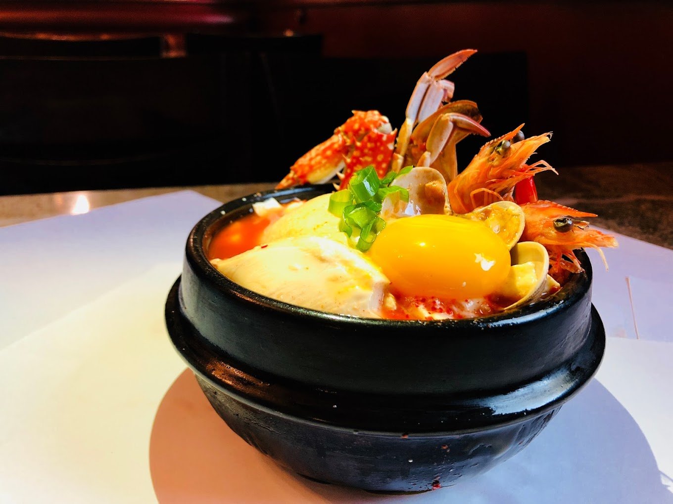 Korean seafood stew with egg yolk and vegetables in a black bowl.