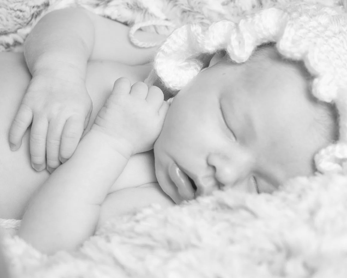 A newborn baby sleeping peacefully on a soft blanket, with tiny hands and face visible.