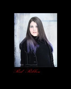 A person with long hair and purple tips wearing a black coat, standing in front of a textured wall. photography by Alana Ranney Maine fine art photography