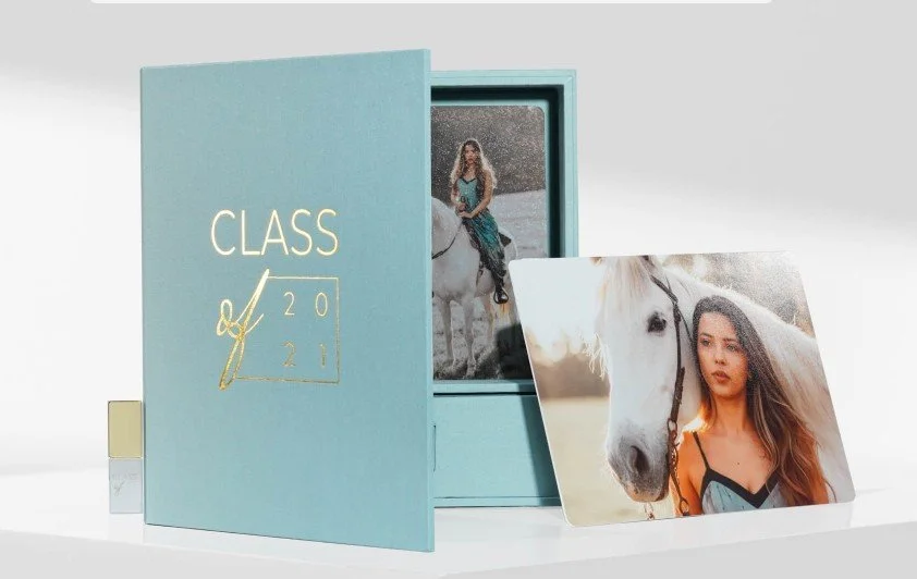 A light blue box with a sliding drawer containing a photo of a woman riding a white horse, and a separate print of a woman with long hair standing beside a horse after rain.